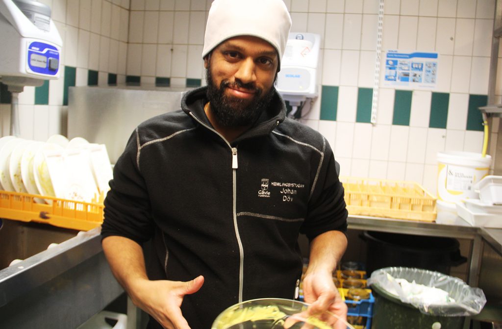 En man som står vid disken i ett restaurangkök med en skål i handen.