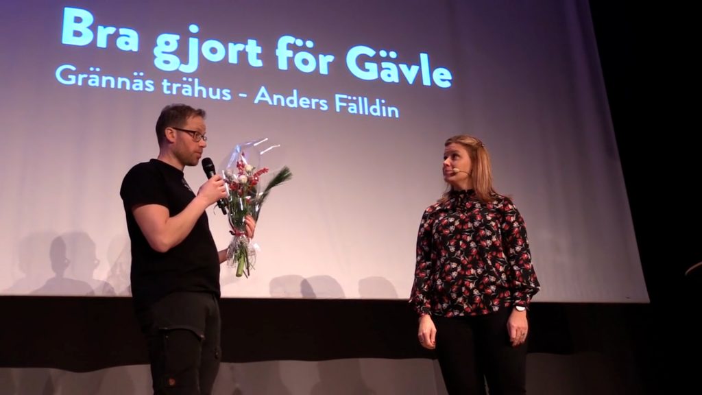 Från näringslivsfrukost. Man som håller i blommor och mikrofon på scen tillsammans med en kvinna.