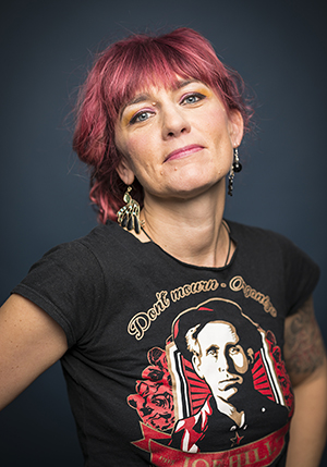 Porträttfoto i studio på Anna Jörgensdotter i t-shirt med tryck på och rosa hår.