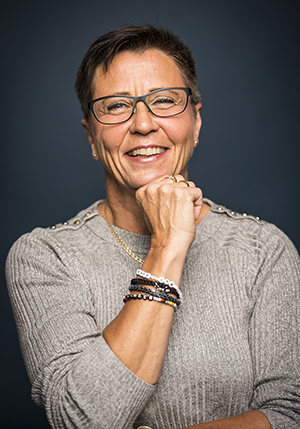 Porträttfoto i studio på Anna Sving-Sjöblom med knuten hand under hakan och på armen syns fyra armband. 