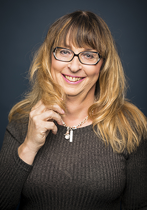Porträttfoto i studio på Erika Wennerström i en brunstickad tröja med fingrar lindat runt hår.
