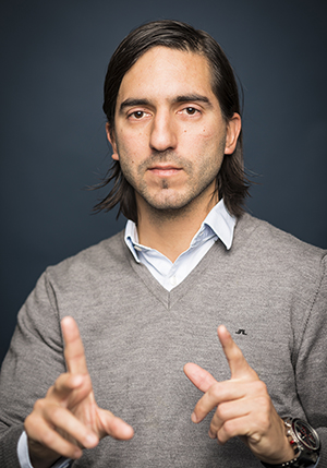 Porträttfoto på Evren Yilmaz i skjorta och tröja över med båda sina spretande fingrarna framför sig.