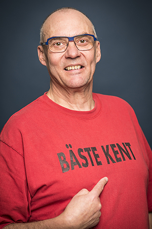 Porträttfoto i studio på Kent Grip i en röd t-shirt med ett finger pekandes mot trycket på böstat där det står Bäste Kent på.