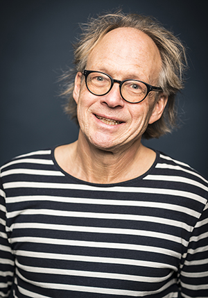 Porträttfoto i studio på Larry Forsberg i randig tröja leendes mot kameran.