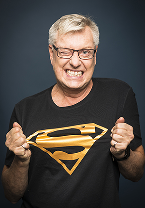Porträttfoto studio på Lars-Åke Wilhelmsson i en superhjälte t-shirt som han drar i.