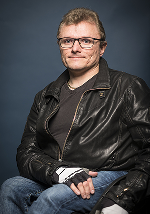 Porträttfoto i studio på Lars-Göran Wadén som sitter i en rullstol med ena handen på låret.