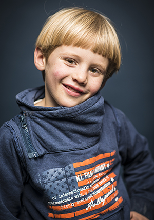 Porträttfoto i studio på Lukas Wallhagen, en liten pojke med lugg i en blå tröja med tryck på.