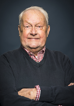 Porträttfoto i studio på Mats Cyril Wiberg i en svart pullover och rödvit rutig skjorta med armarna i kors.