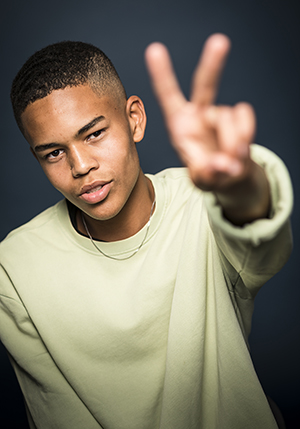 Porträttfoto i studio på Milton Ndiaye, ung kille som gör v - tecken med ena handen mot kameran.