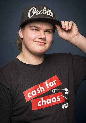 Porträttfoto i studio på Rasmus Eldebrandt i svart t-shirt med rött tryck på som håller i kepsen på huvudet med ena handen.
