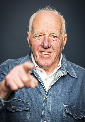 Porträttfoto i studio på Werner Baumgartne, äldre man i jeansskjorta som pekar mot kameran.