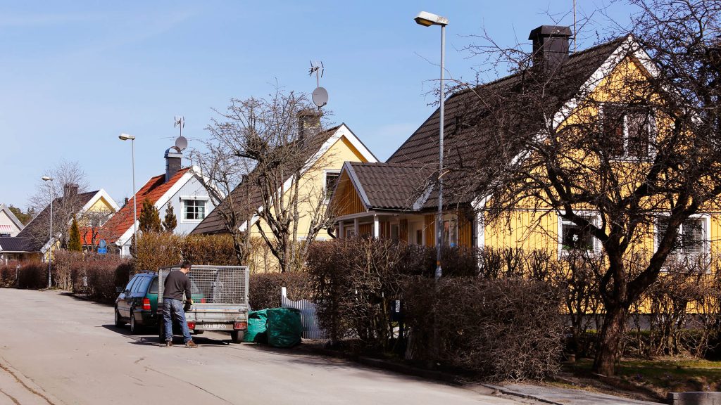 En man vid släpkärra kopplad till personbil framför villa i svenskt villaområde gör klart att lasta avfall.