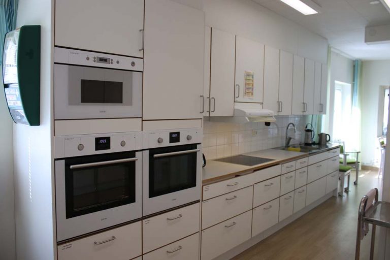 Köksavdelning med vita köksluckor, ugnar och micro.