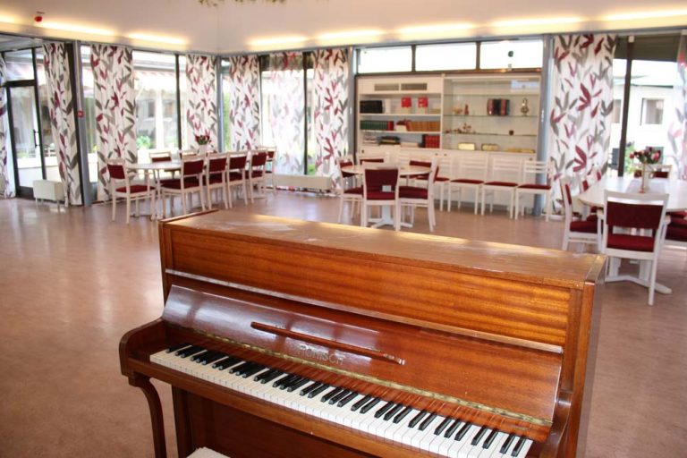 Stort sällskapsrum med piano och sittmöbler vid entrén