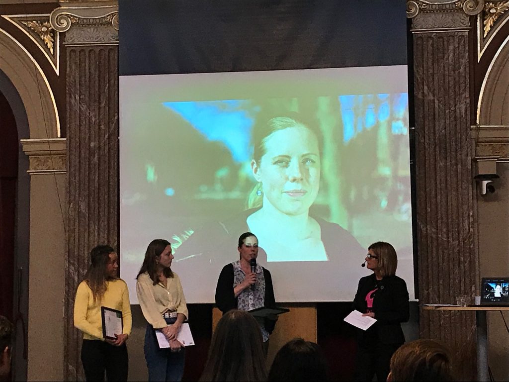 Fyra kvinnor på en scen med en projektor med bild på en kvinna i bakgrundern