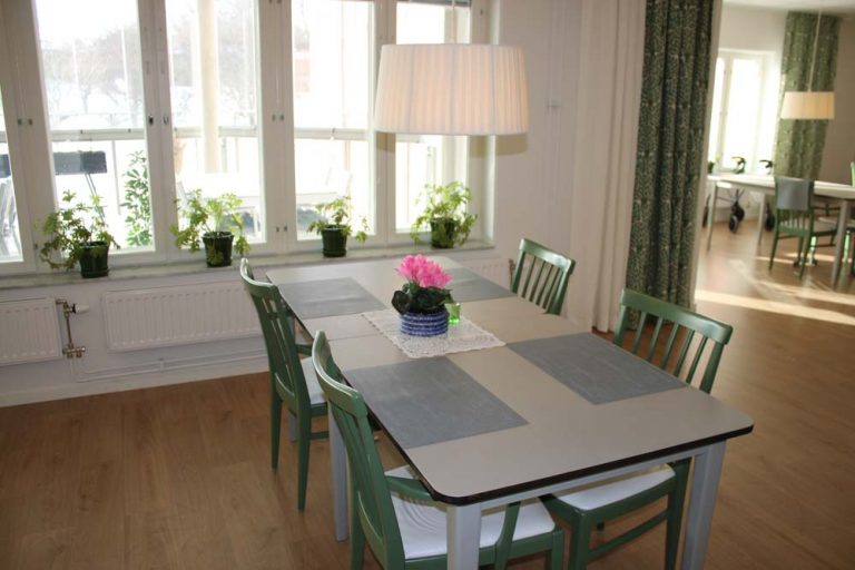 Matrumsdel med gröna pinnstolar och blomma på bordet.