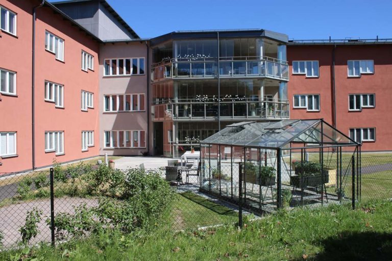 Växthuset på gården. I bakgrunden det röda tegelhuset med stora balkonger.