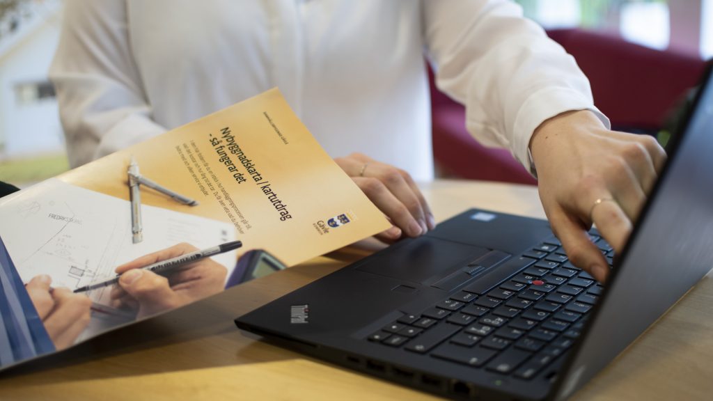 Bygglovsbroschyr, en laptop och en person som pekar på datorskärmen