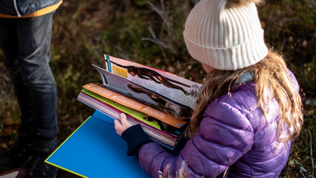 En liten flicka sitter och bläddrar i en tidning utomhus