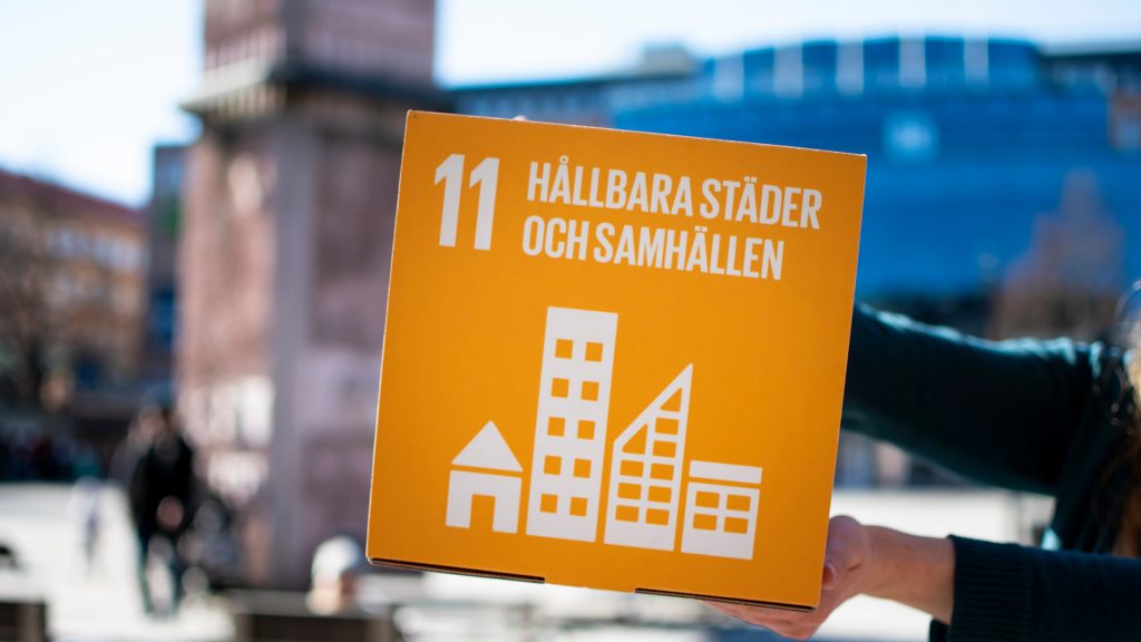 En skyld med texten Hållbara städer och samhällen hålls upp på Stortorget i Gävle.