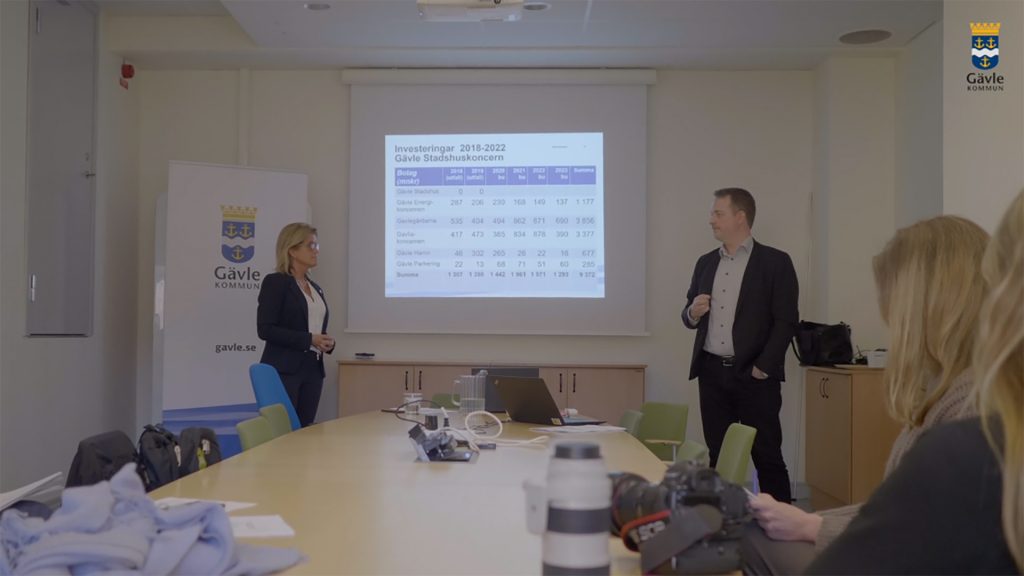 Två personer som står framför en projektorduk och talar inför folk.