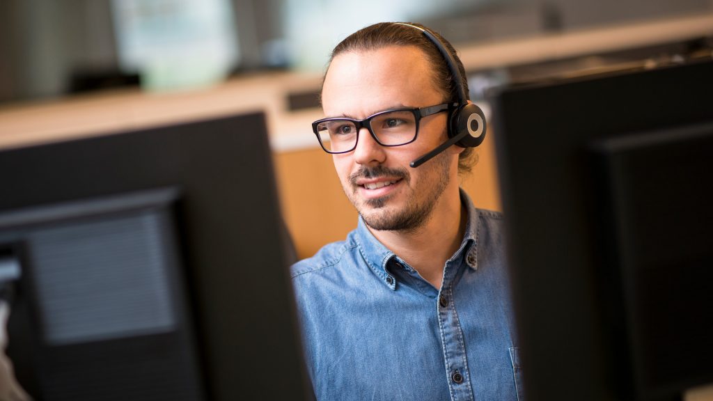 Man pratar i telefon med headset och sitter framför två datorskärmar.