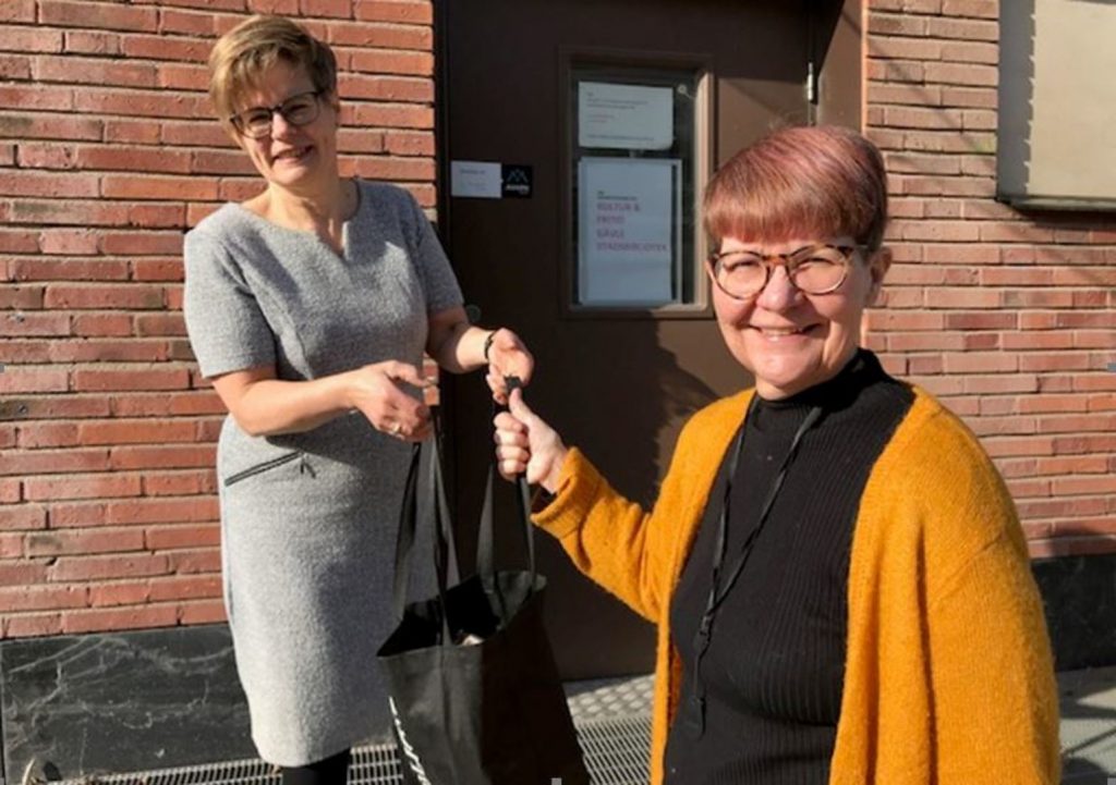 En kvinna överlämnar en bokkasse till en annan kvinna.