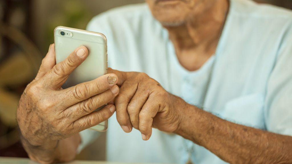Äldre man sitter och trycker på en mobiltelefon.