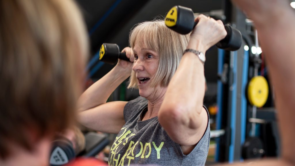 Äldre kvinna tränar på gym med hantalar.