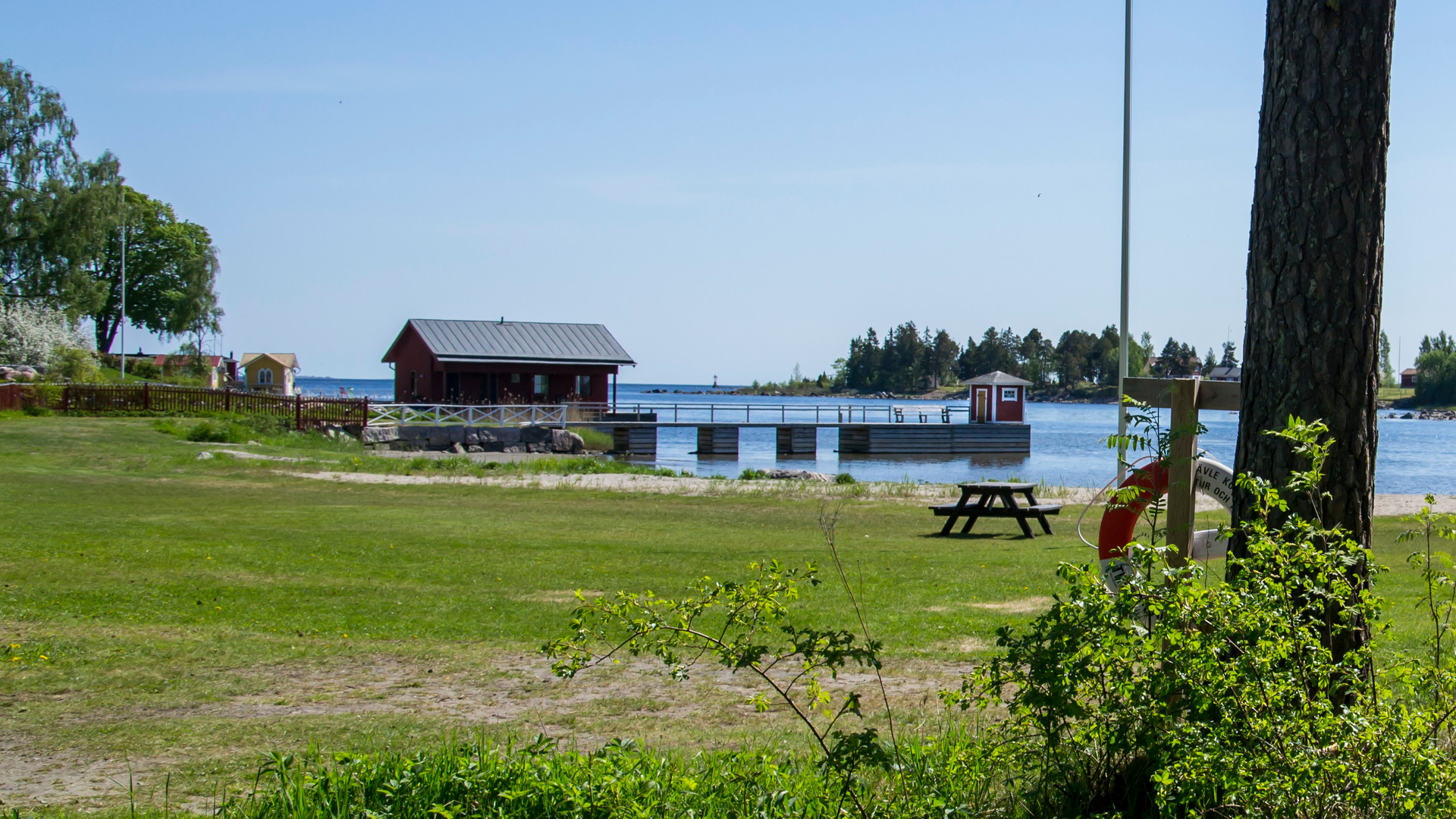 Gräsmatta, sandstrand och vatten vid Bönaviken