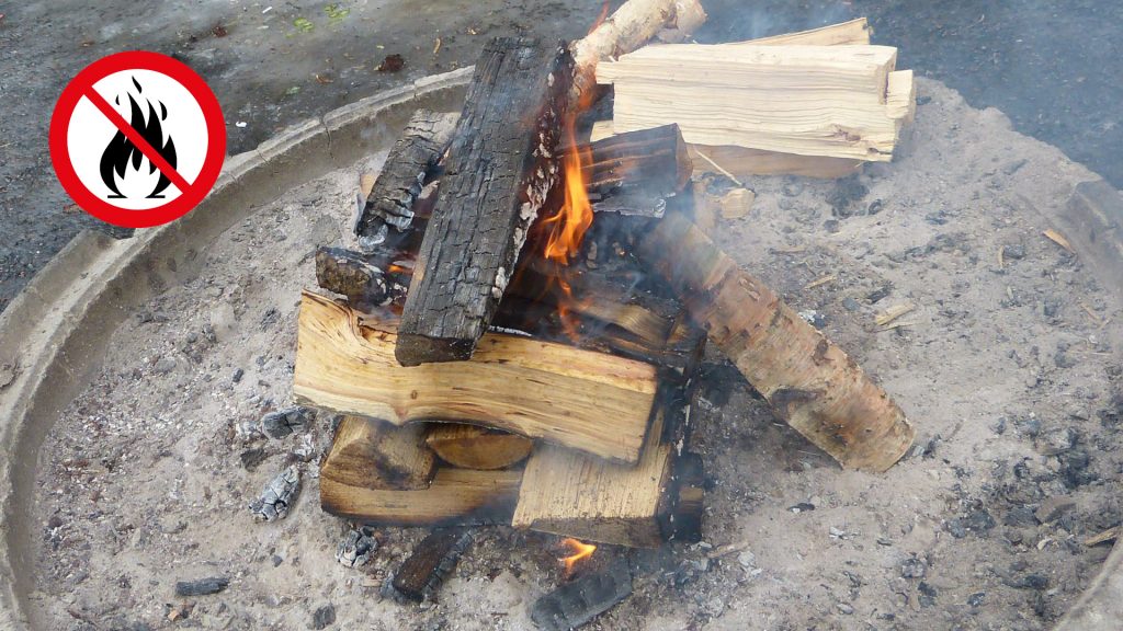 Eldstad med brinnande ved och symbol för eldningsförbud