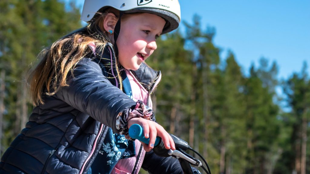En som flicka cyklar med skog i bakgrunden
