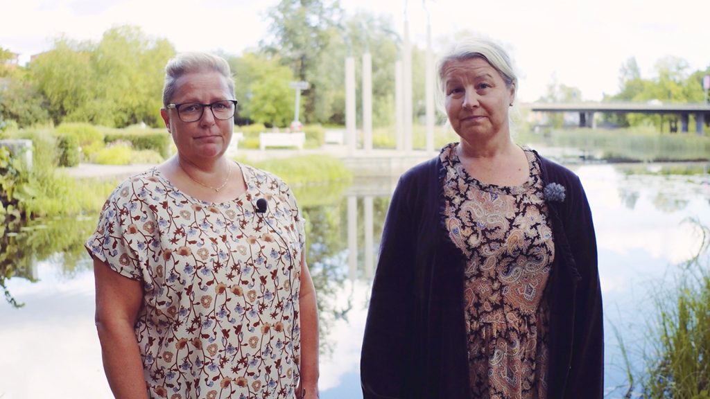 Två kvinnor stående vid Gavleån med Musicerande änglarna i bakgrunden