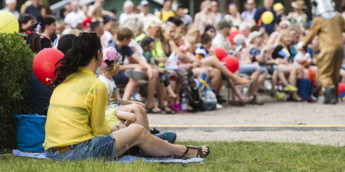 Sittande folksamling i en park som tittar på en föreställning.