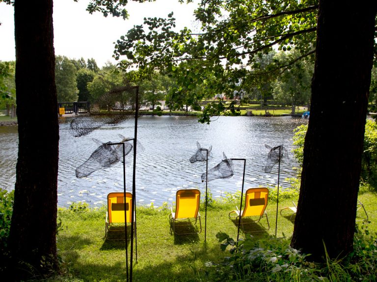 Solstolar och hovar på en gräsmatta framför en sjö.