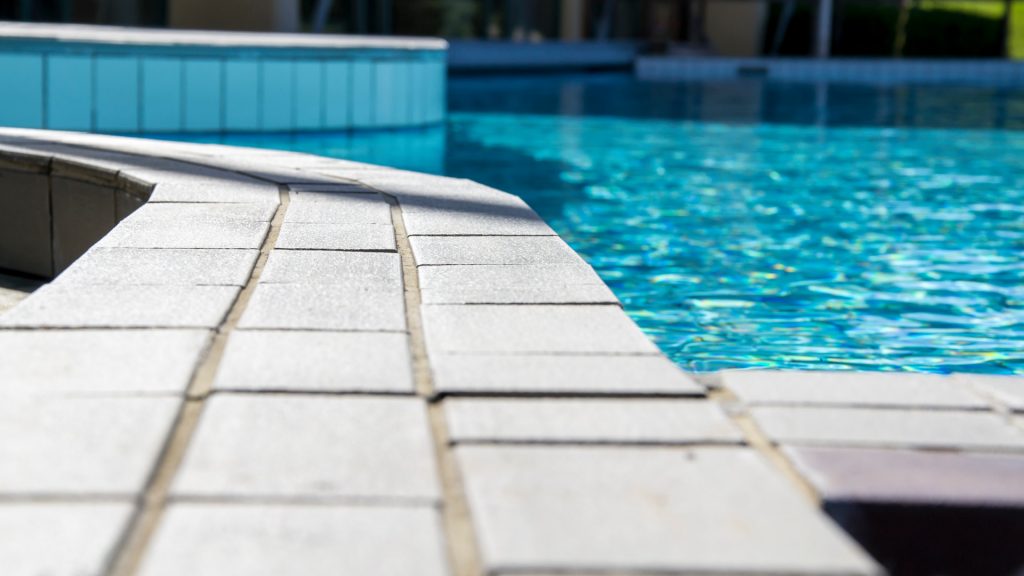 Poolkant ur grodperspektiv med en liten del av poolvatten i poolen på sidan.