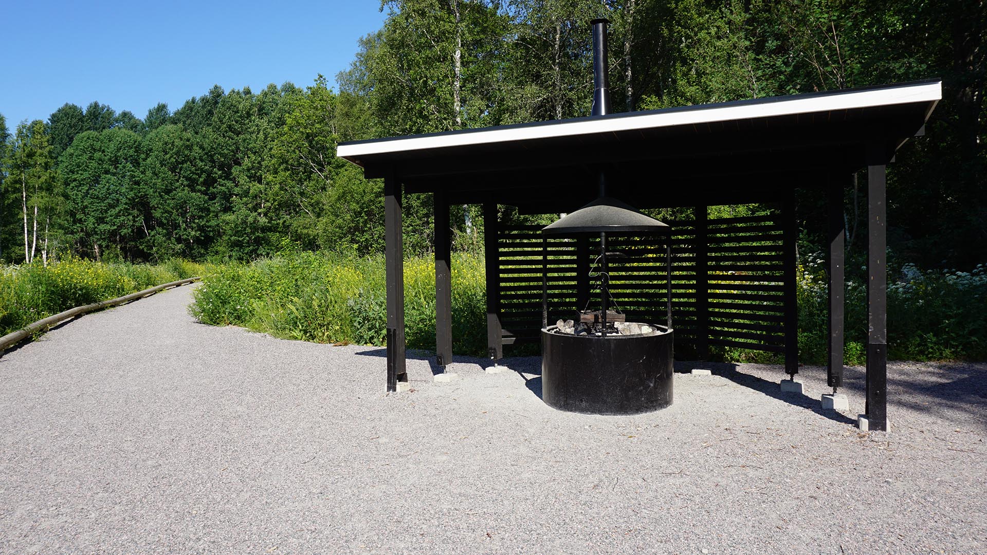 Grillplats på en ett grusområde med skog och grönska i bakgrunden.