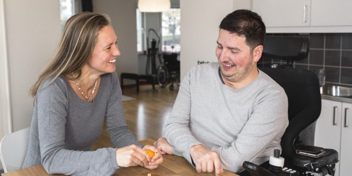 Assistent och brukare sitter vid köksbordet och skrattar.