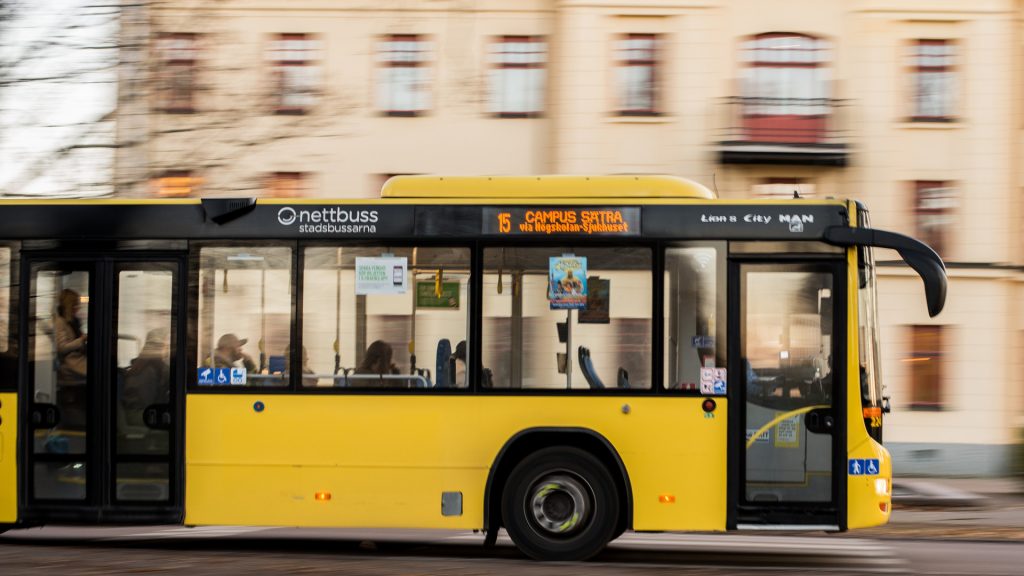 Stadsbuss åker förbi ett hus i bakgrunden
