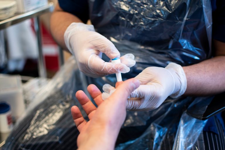 En person utför provtagning genom stick i fingret på en patient