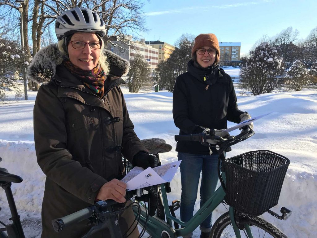 Två kvinnor stående med varsin cykel på snöigt underlag.