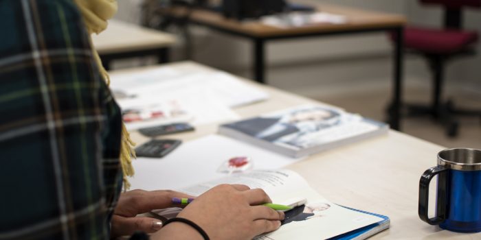 En person sitter vid ett bord och har händerna på en bok ihållande en penna.