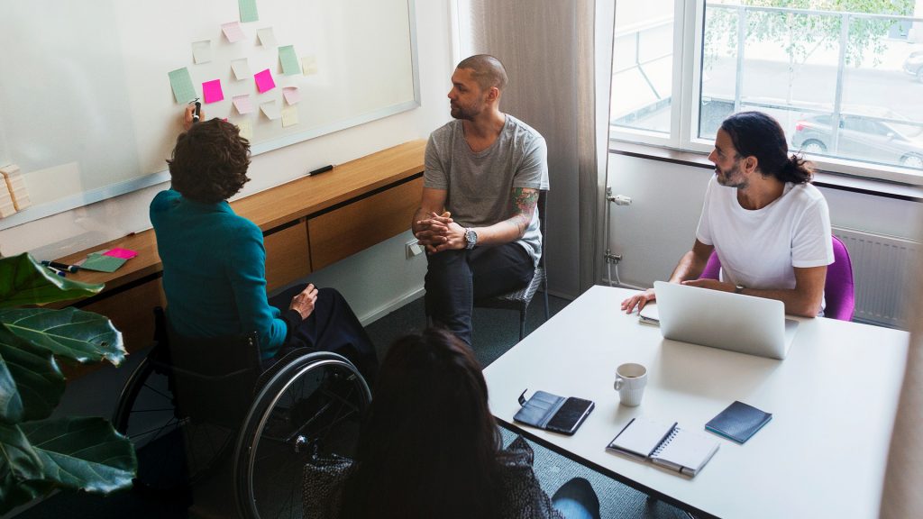 4 personer sitter i ett konferensrum med whiteboardtavla med postit-lappar på.