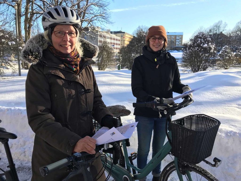 Två kvinnor stående med varsin cykel på snöigt underlag.