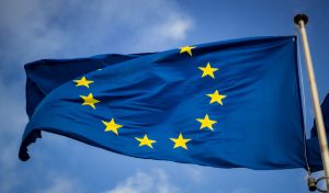 EUflagga i toppen av en flaggstång mot blå himmel.