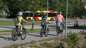 Tre barn och en vuxen kvinna cyklar på en cykelväg i sommarmiljö