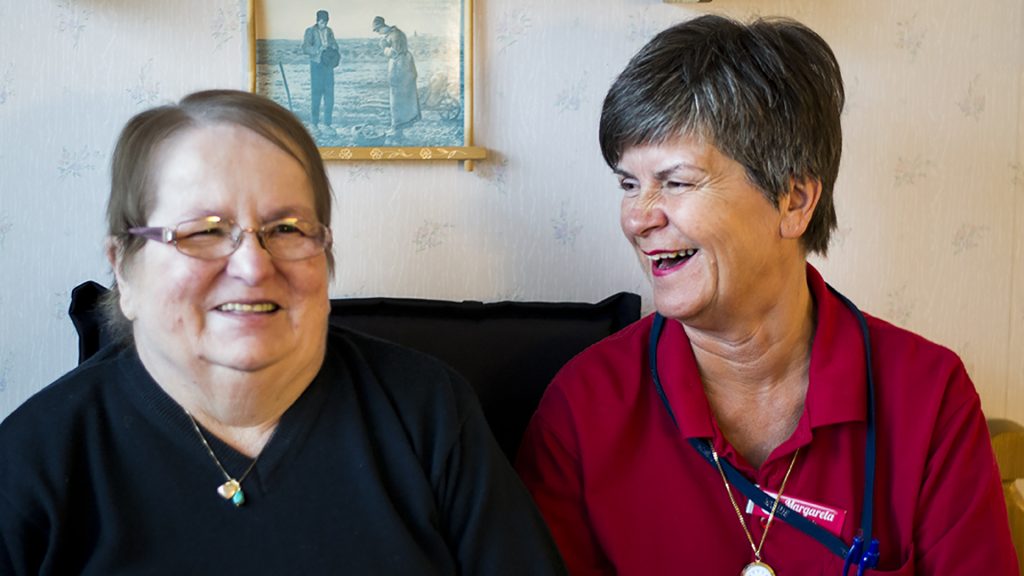 En brukare med hemtjänstpersonal som sitter bredvid varandra och skrattar