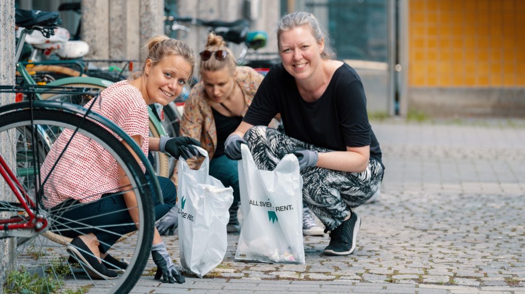 Tre personer sitter på huk och plockar skräp.
