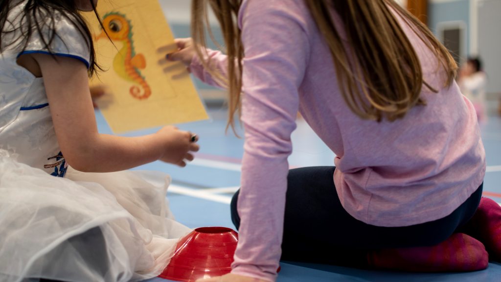 Barn som sitter på ett gymnastiksalsgolv och tittar på en teckning