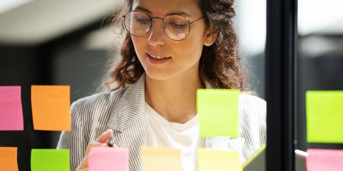 Ung kvinna skriver på post-it-lappar som sitter på glasvägg.